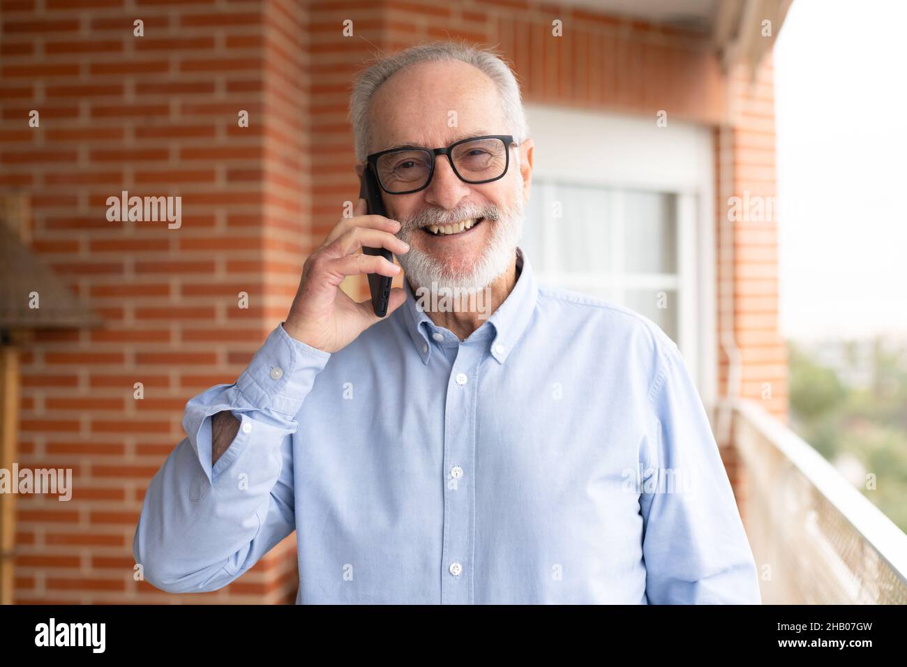 Smiling senior man talking on mobile phone in the terrace at home. Stock Photo