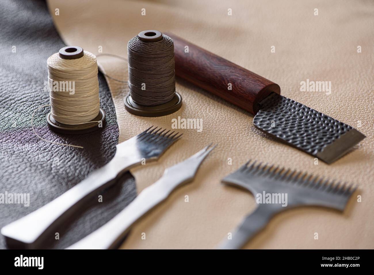Shoemaker's tools laying on piece of beige and brown genuine leather in workshop. Workplace of shoemaker for sewing handmade shoes. Selective focus. Stock Photo