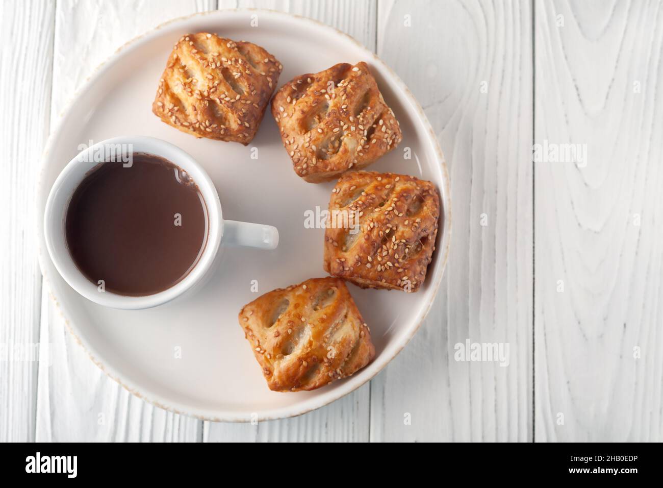 On a white wooden table there is a mug with hot chocolate and fresh aromatic puffs. Stock Photo