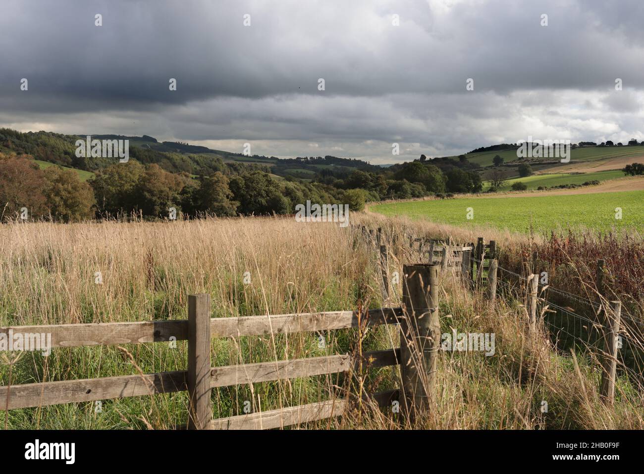 Farmland in the Scottish highlands. A wooden fence in the foreground. Cloudy sky. Stock Photo