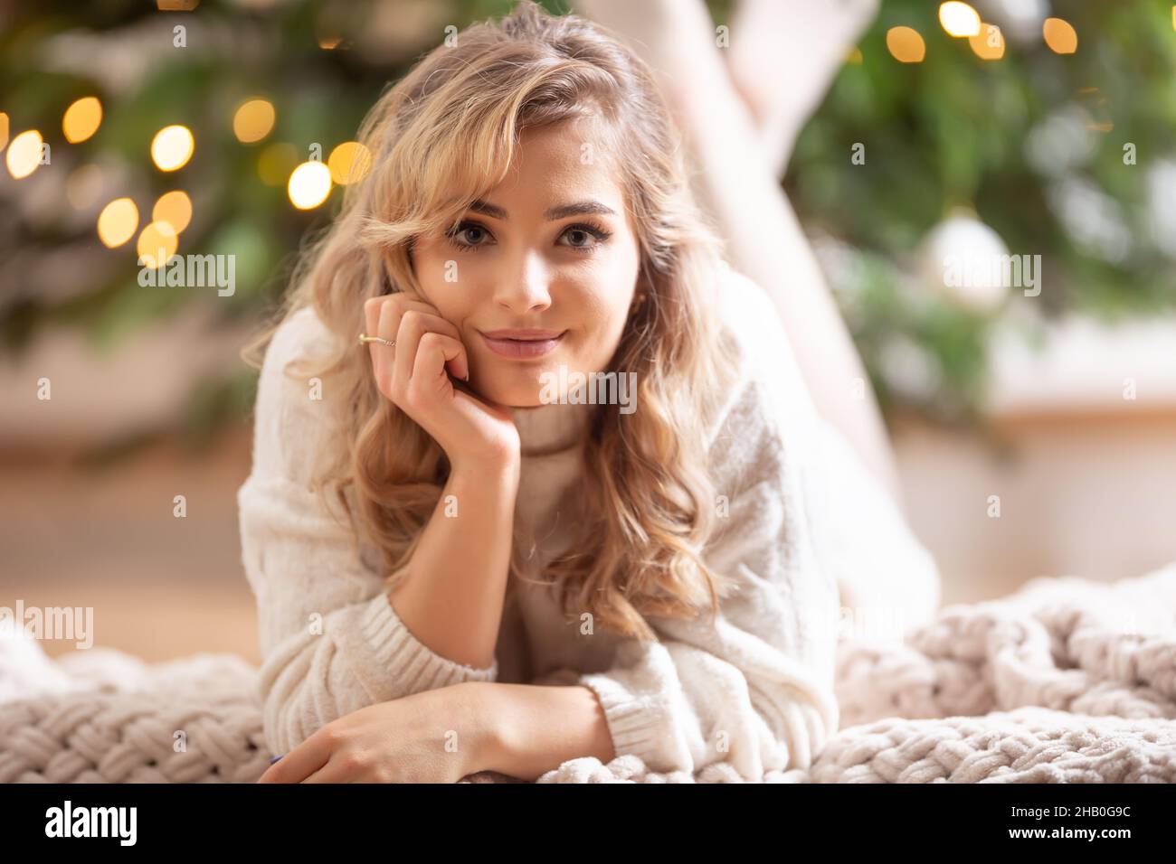 Young beautiful smiling blonde lying on a blanket next to a Christmas tree. Stock Photo