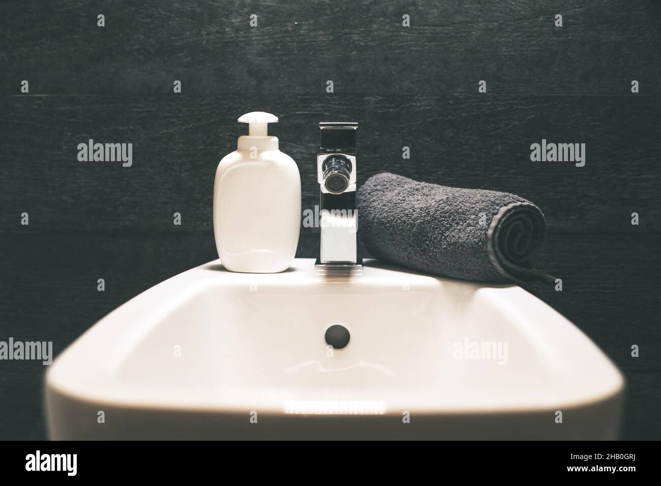 Closeup view of a bidet with rolled up towel, soap dispenser. Modern