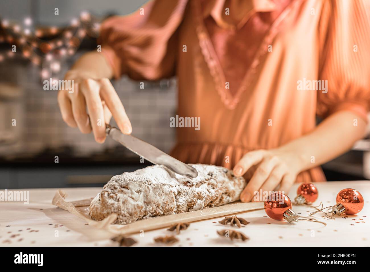 cut festive traditional German Stollen pie into pieces. girl in festive dress cuts stollen with knife in kitchen on christmas eve Stock Photo