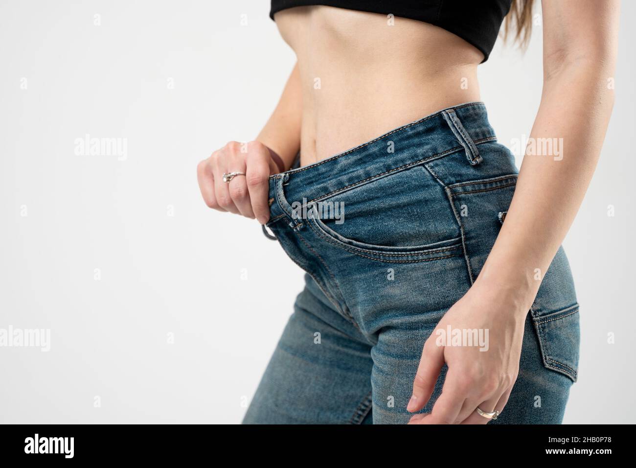 Cropped portrait of young female with flat belly and slim waist standing on  blank studio wall. Brunette woman wearing denim pants showing her beautiful  fit body. Lifestyle and people concept. Photos
