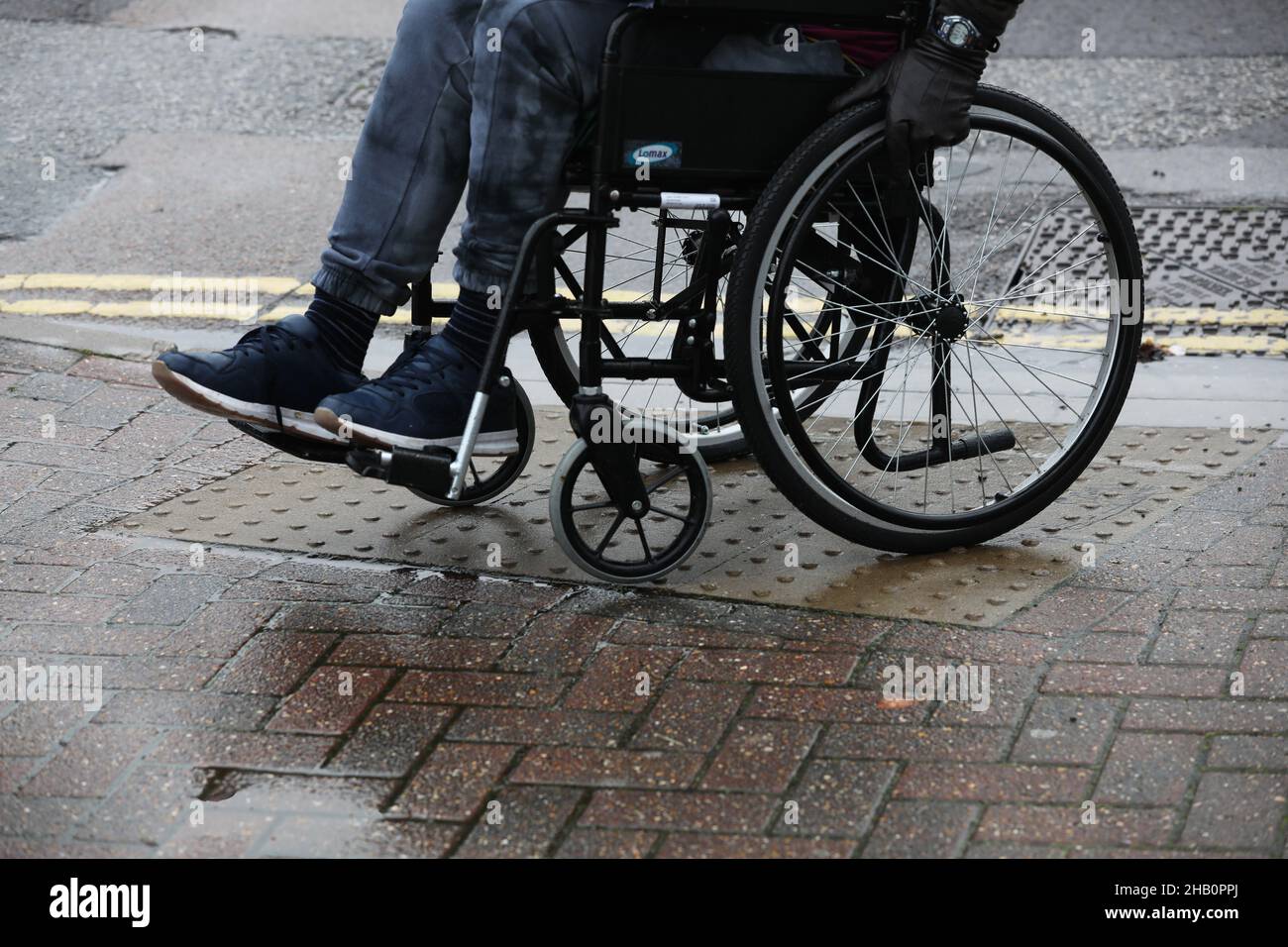 A man in a wheelchair pictured using it along an uneven path in London, UK. Stock Photo