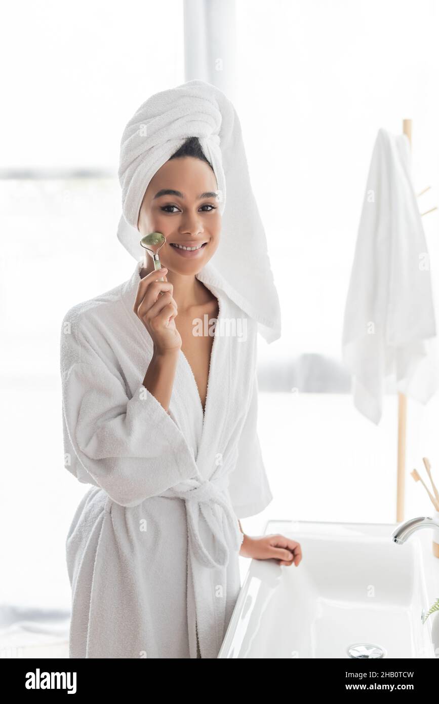 happy african american woman in bathrobe and towel massaging face with ...