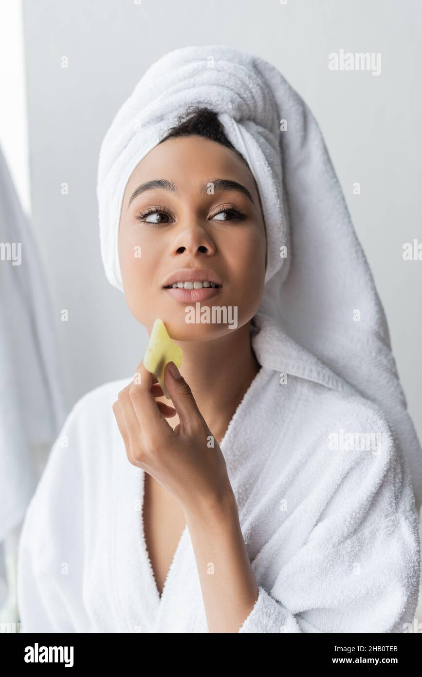 pretty young african american woman in white towel massaging face with ...