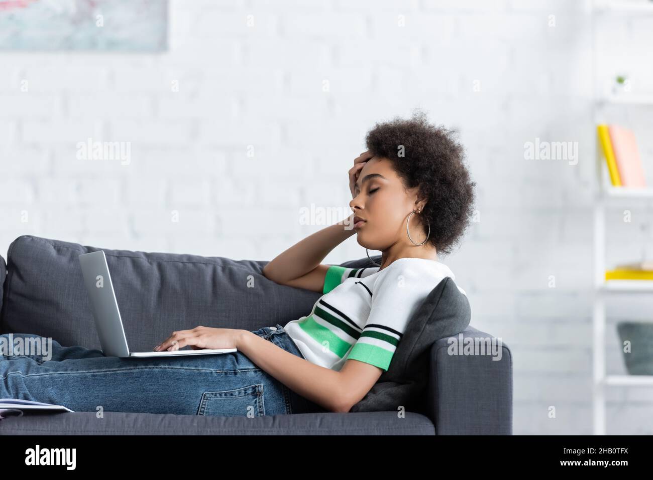 sleepy african american woman sitting with laptop on couch Stock Photo ...