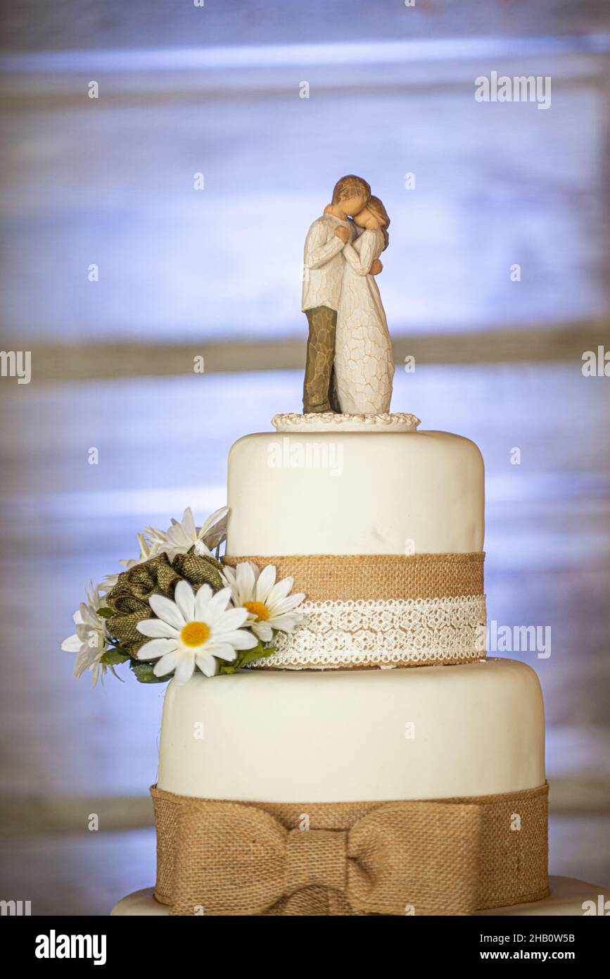Amazing three tier wedding cake with canvass lace and bows and sunflowers on wood bark stand and wood door background Stock Photo