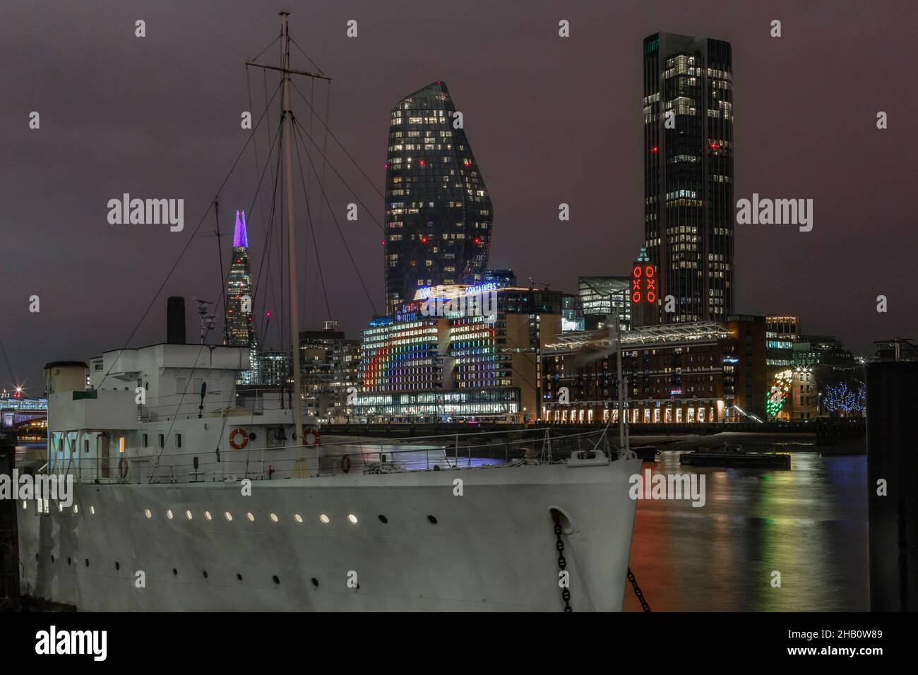 HMS Wellington on river Thames with other famous landmarks on the south bank in the background. Stock Photo