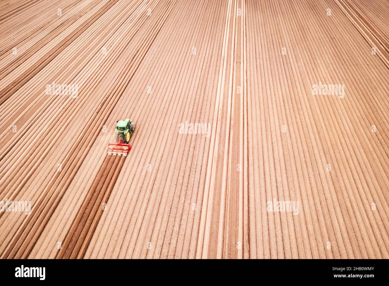 Lonely tractor on agricultural field with rows of plowed soil. Agricultural fields prepared for planting crops, topdown view. Industrial agriculture concept. Drone photography Stock Photo