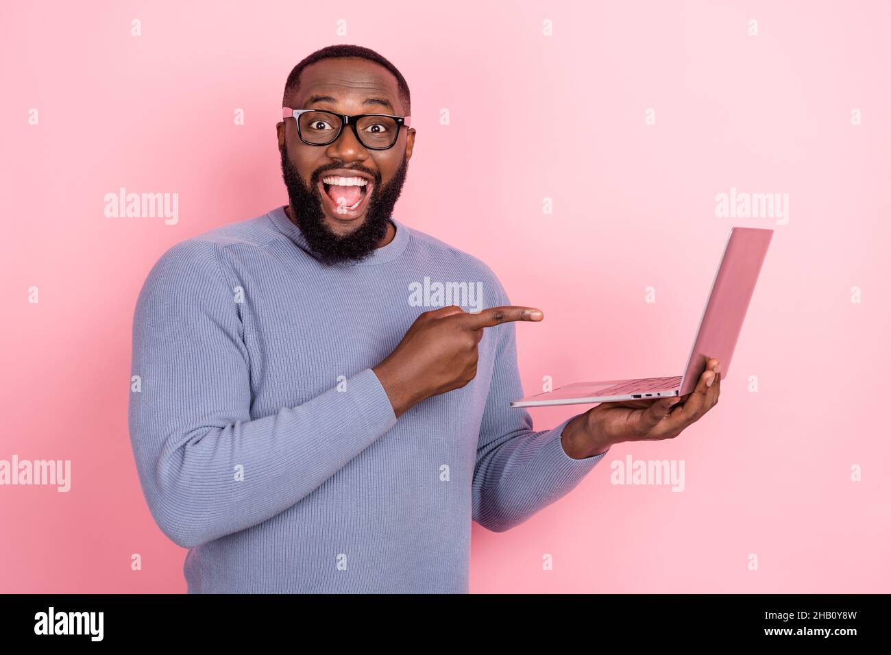 Photo of shocked afro guy wear grey pullover glasses pointing modern device isolated pink color background Stock Photo