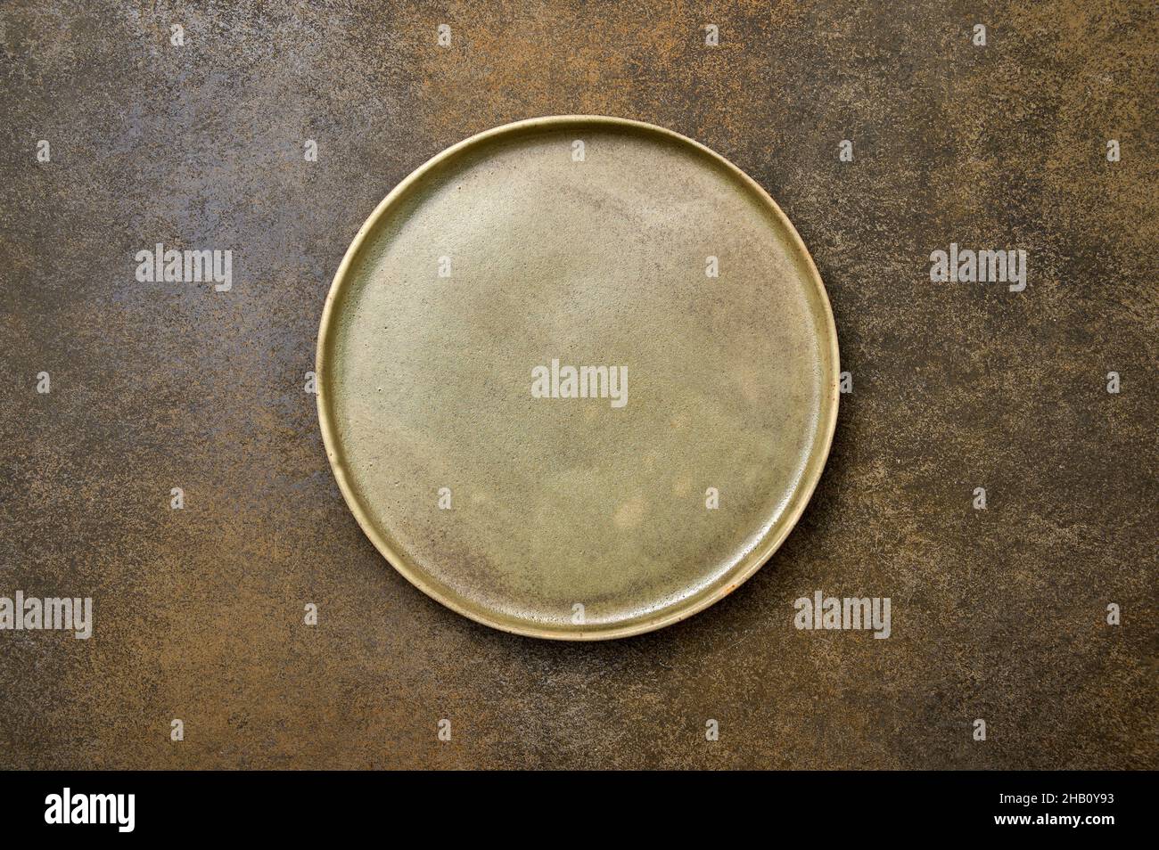 Empty green rustic ceramic plate with black rim on brown rustic background, flat lay, copy space Stock Photo