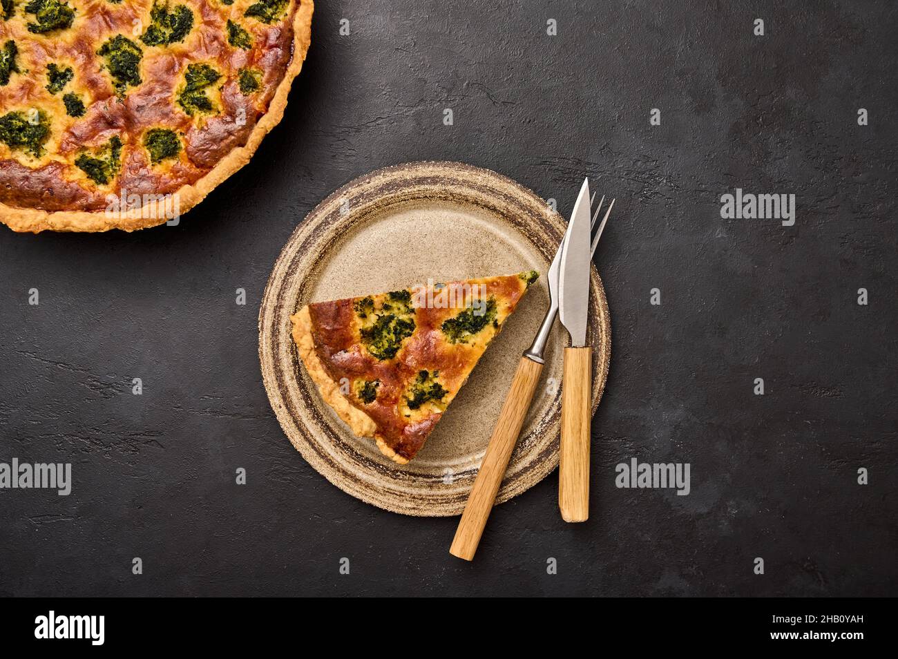 Piece of quiche tart on ceramic rustic plate with knife and fork on black graphite background. Top view Stock Photo