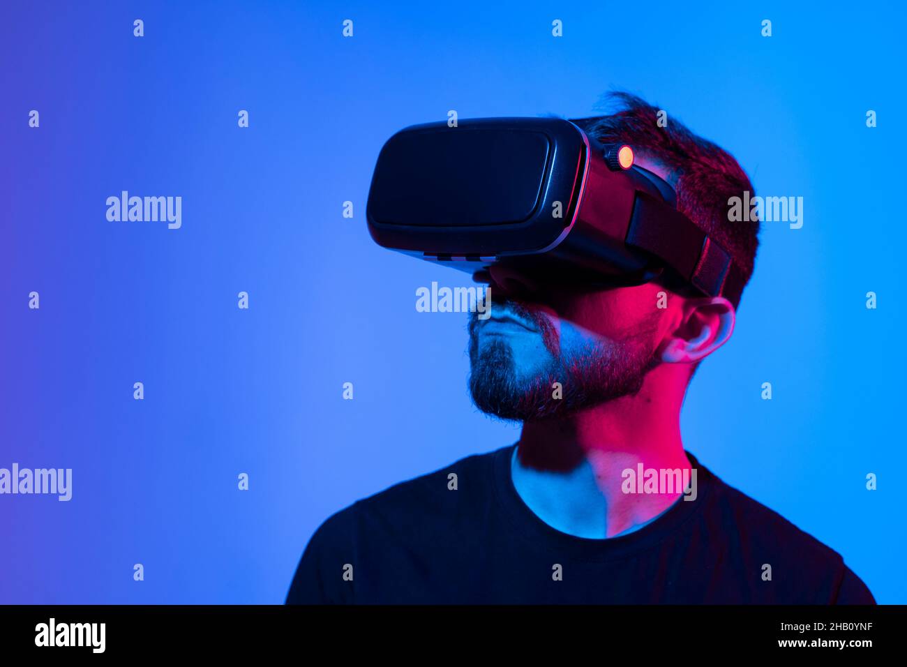 Portrait of man using VR headset while playing a video game in dark interior illuminated neon light. Close-up futuristic googles with colored light. Stock Photo