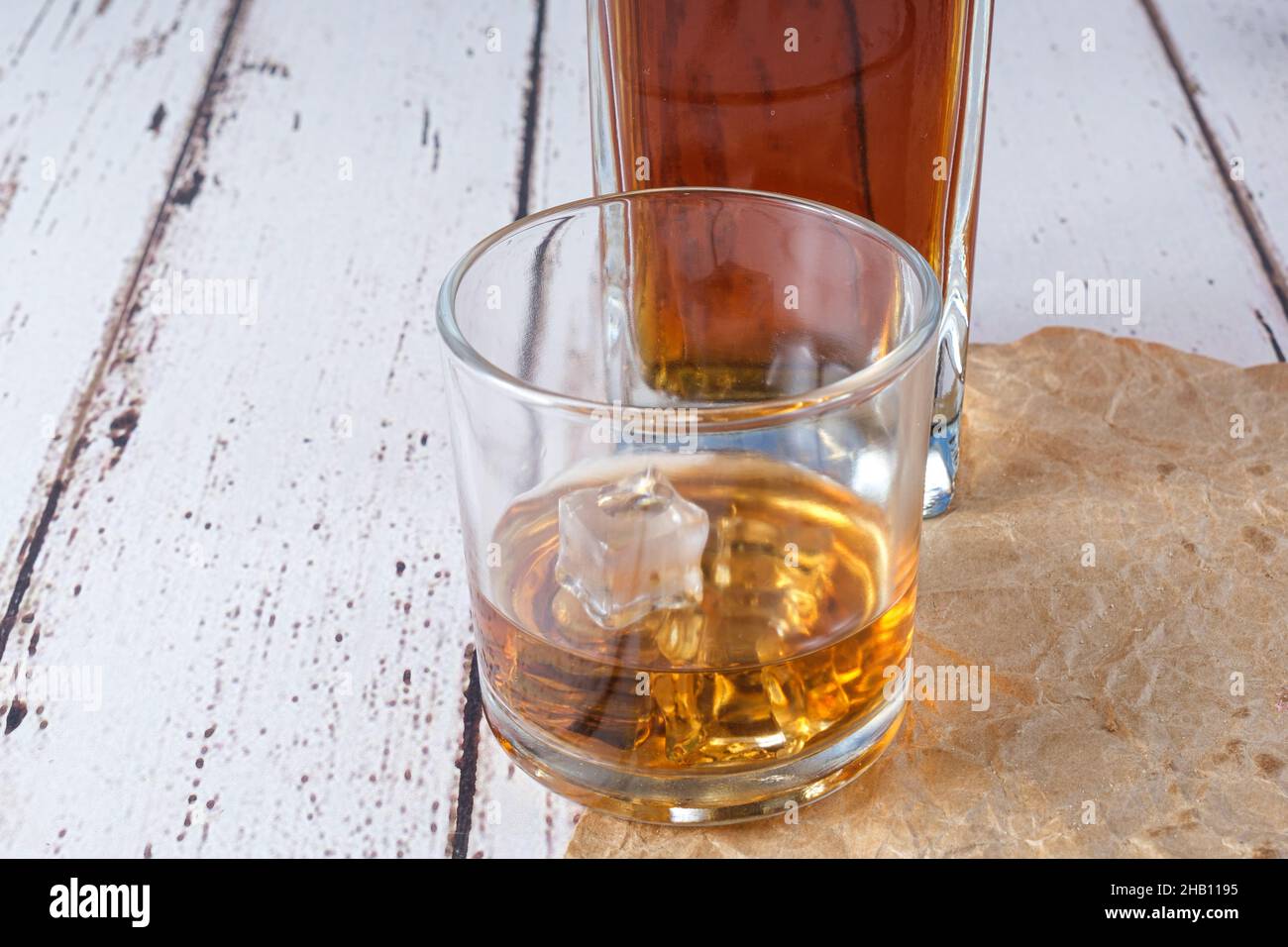 Glass of whiskey with ice on brown paper. In the background, a bottle of whiskey. Stock Photo