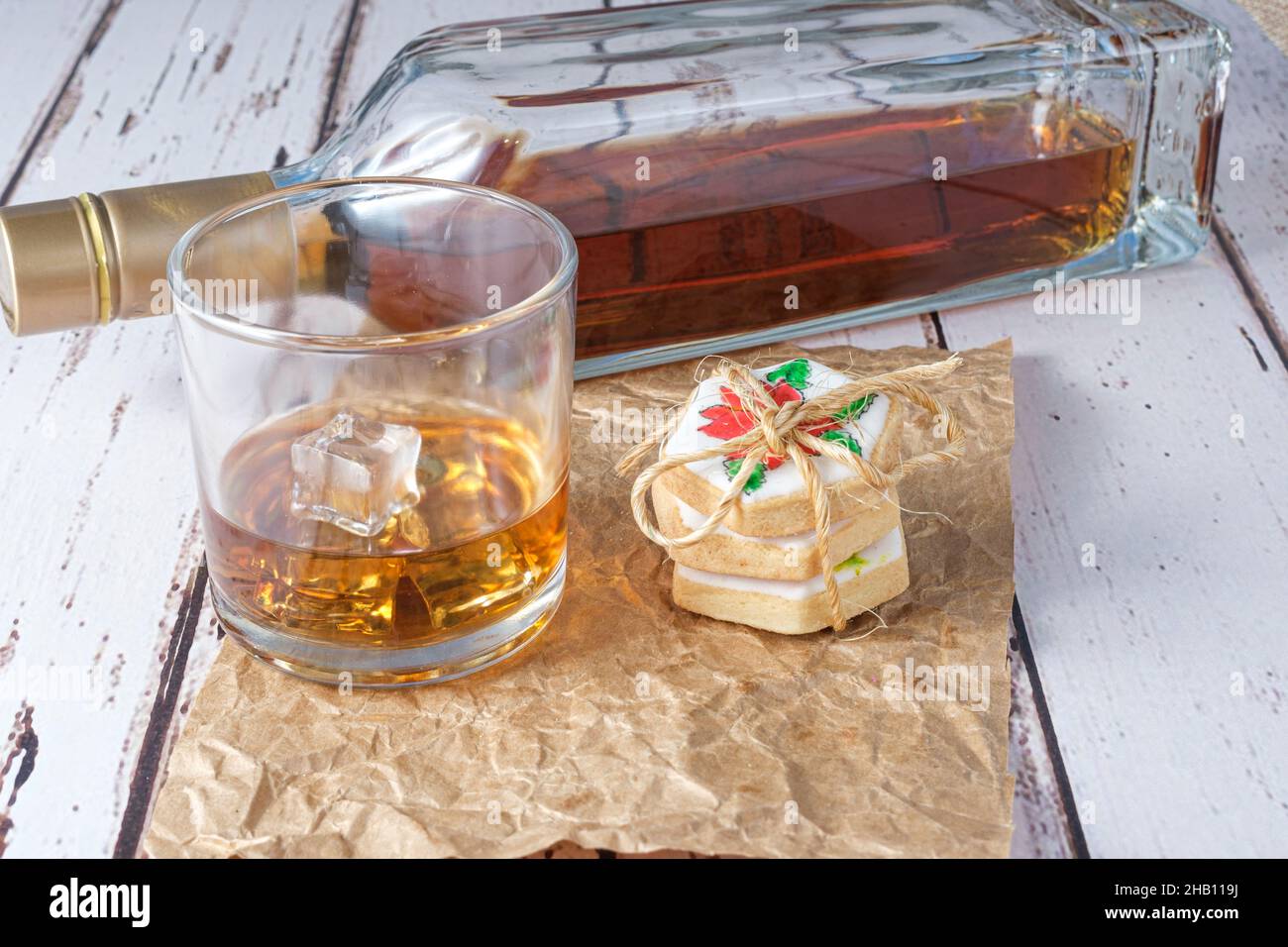 Glass of whiskey with ice on brown paper next to biscuits with a sisal bow. Stock Photo