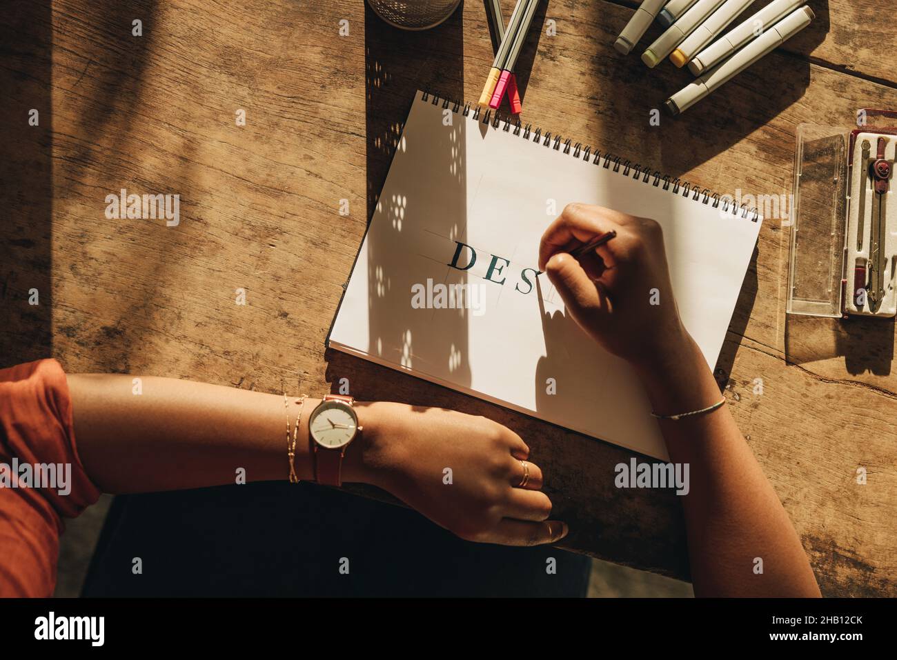 Female freelancer drawing the word ''DESIGN'' while sitting at her workstation. High angle view of a female graphic designer working on a new project. Stock Photo