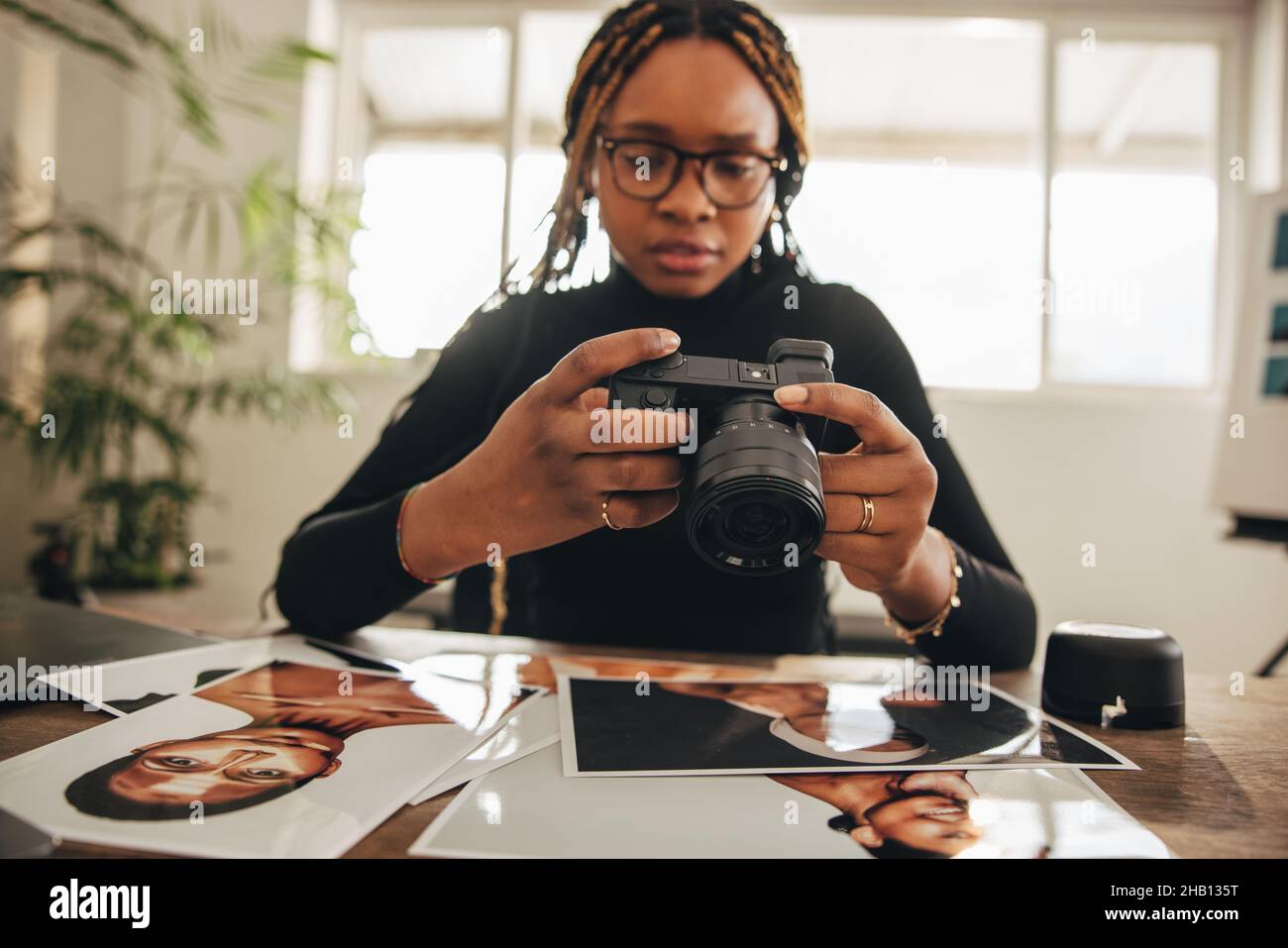 Photographer holding a dslr camera in her home office. Self-employed photographer working with photographs at her desk. Creative female freelancer wor Stock Photo