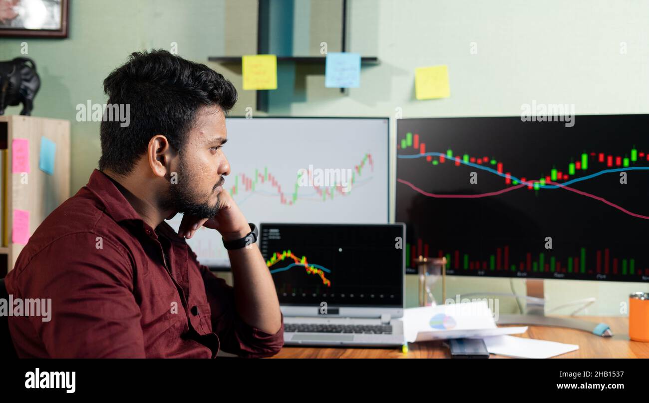 Thinking Young man while trading in front of stock market charts on monitor - concept of risk in investing money on equity shares and disappointed Stock Photo