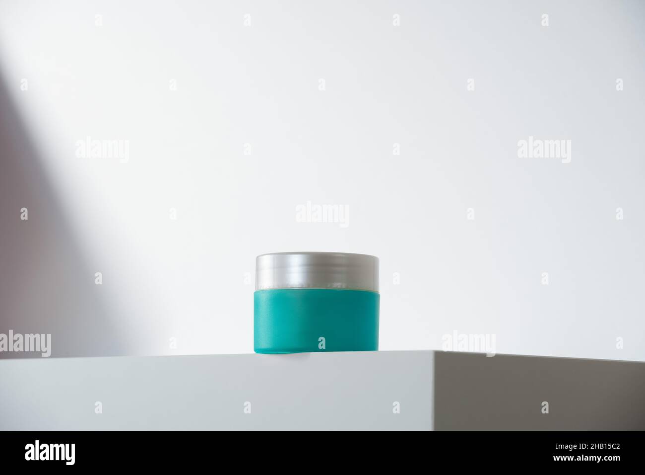 vibrant teal cream pot with silver lid on white podium and background. Modern geometric minimalism in self-care beauty. Hero shot Stock Photo
