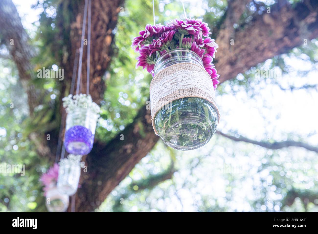 Various flowers in mason jars hanging from trees over wedding ceremony