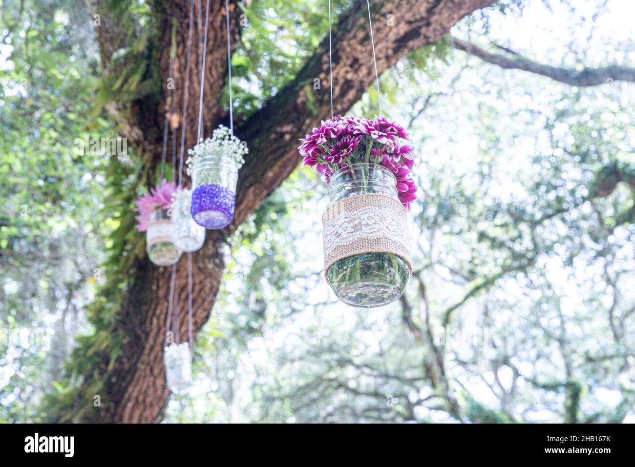 Various flowers in mason jars hanging from trees over wedding ceremony