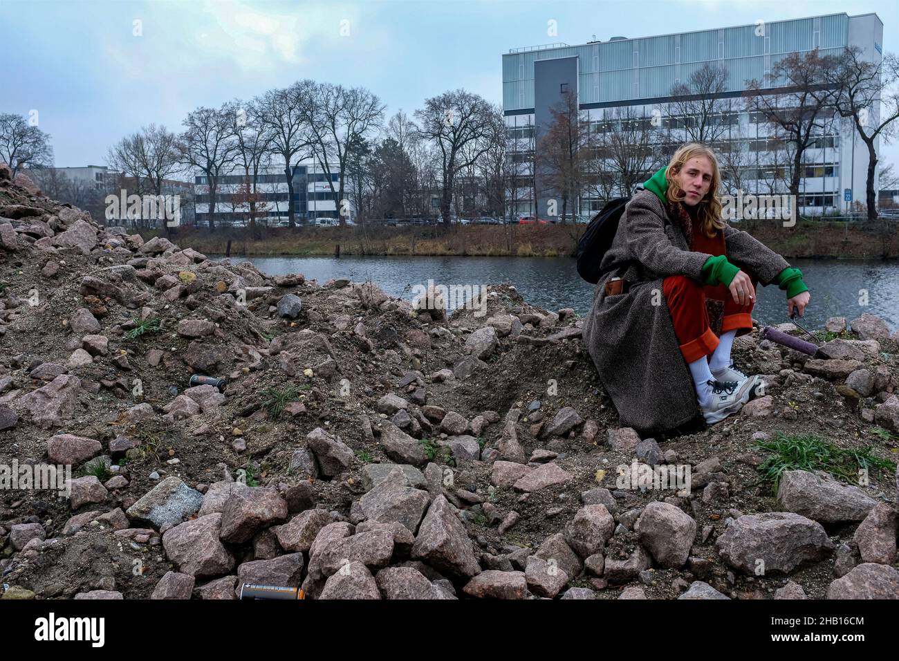 Berlin, Germany. Young adult punk dude sitting on a pile of rock near a huge graffity place, somehwere in Spandau. Stock Photo
