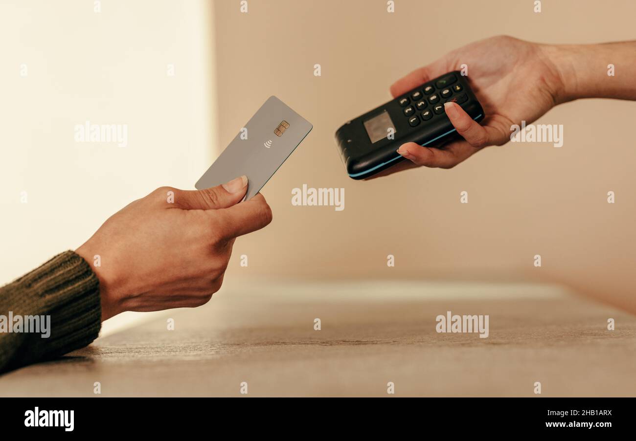 Woman's hand tapping a credit card on a contactless card reader. Unrecognizable female customer paying with a credit card at the checkout counter. Stock Photo