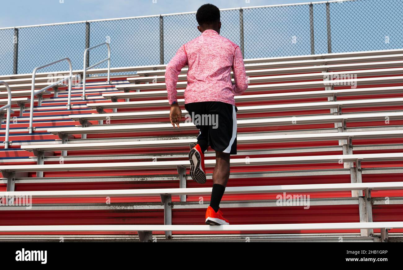 Rear view of on African American runner running up red stadium bleachers. Stock Photo