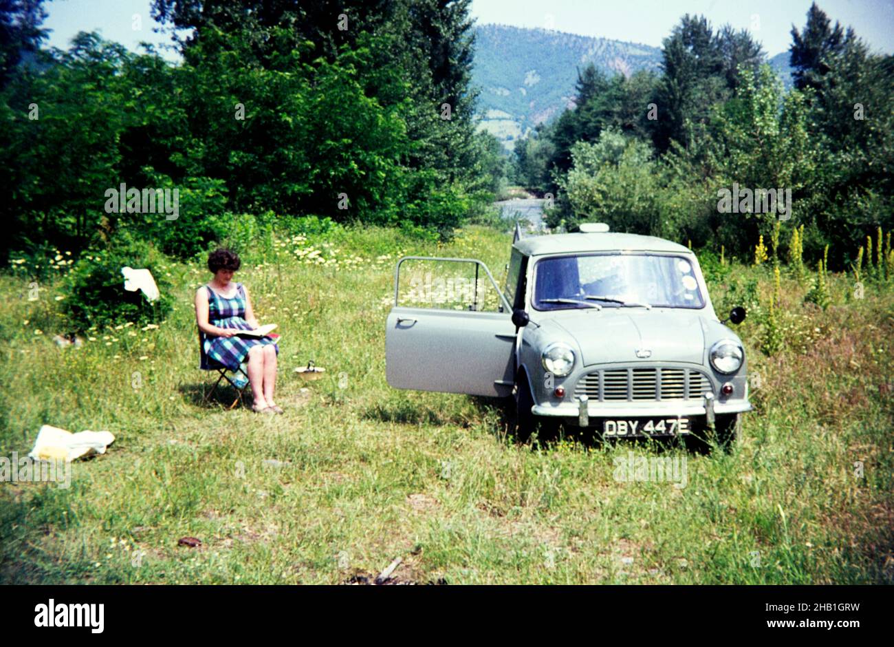 Woman reading by Austin Mini van camping in countryside area, Romania, eastern Europe 1967 Stock Photo