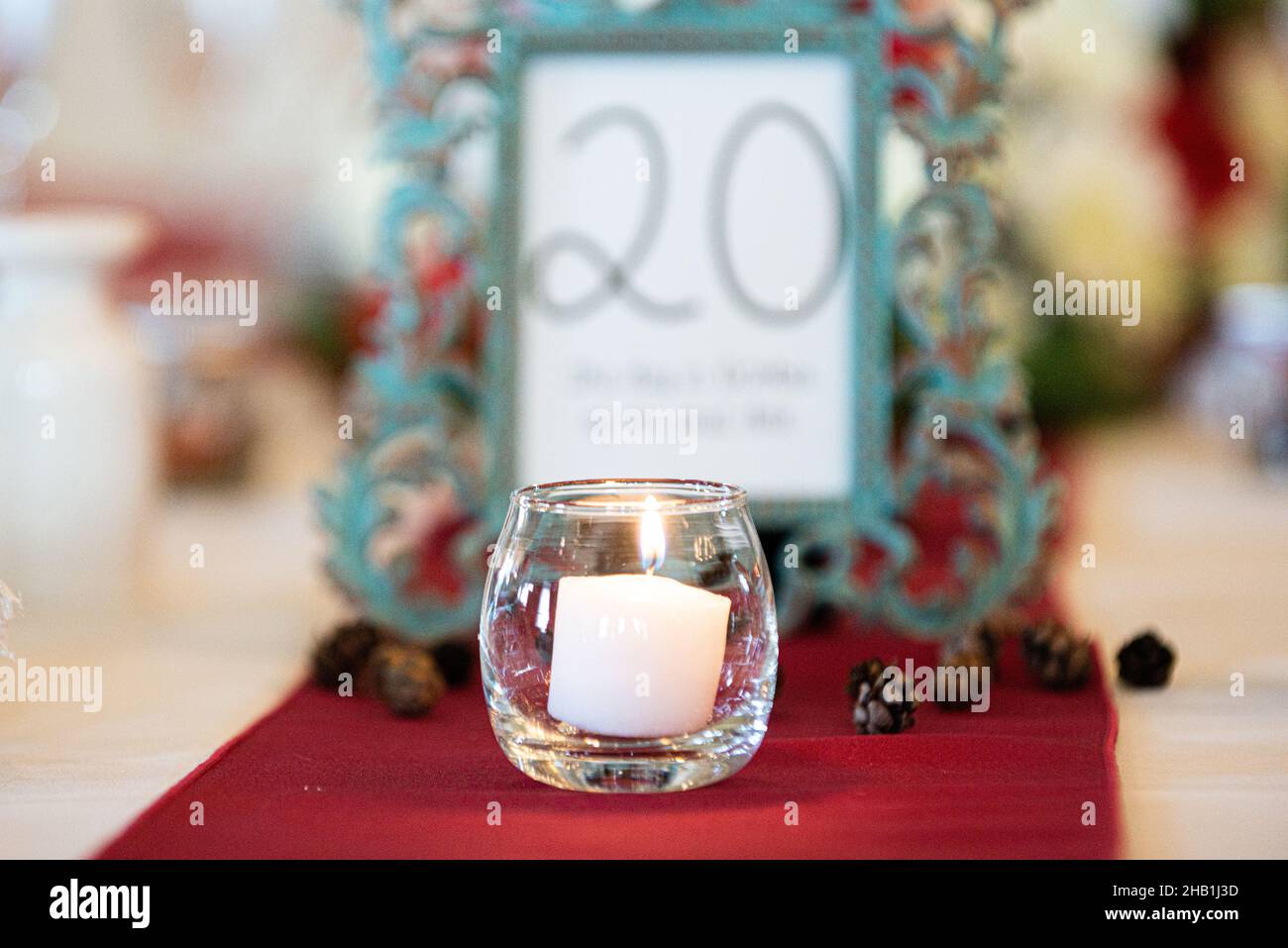 Glass candle holder with white lit candle centerpiece on red table cloth wedding reception Stock Photo