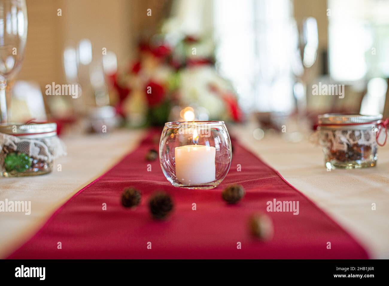 Glass candle holder with white lit candle centerpiece on red table cloth wedding reception Stock Photo