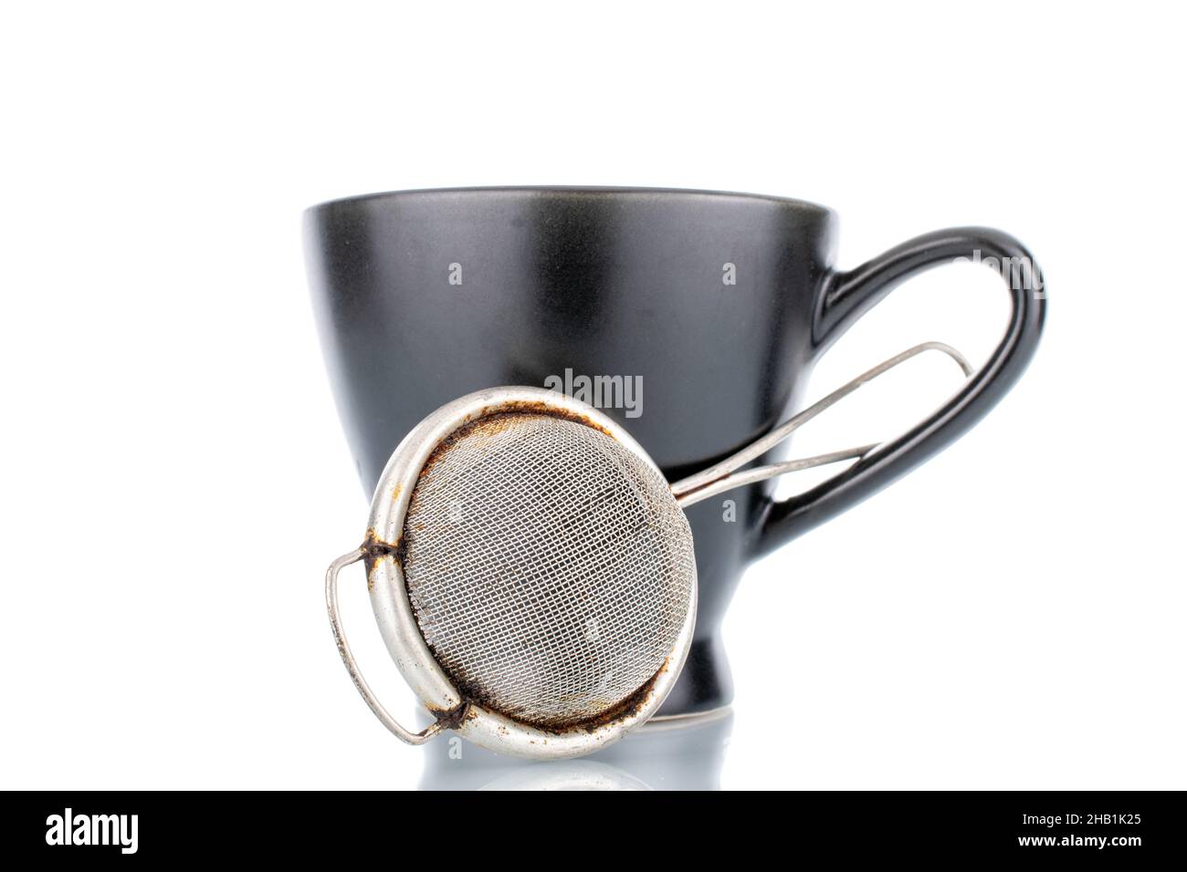 One metal tea strainer and a black ceramic cup, closeup, isolated on