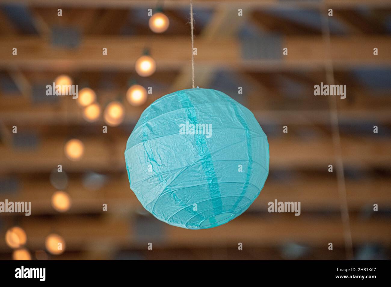 Blue round paper lantern hanging from wood beam ceiling with bokeh Stock Photo