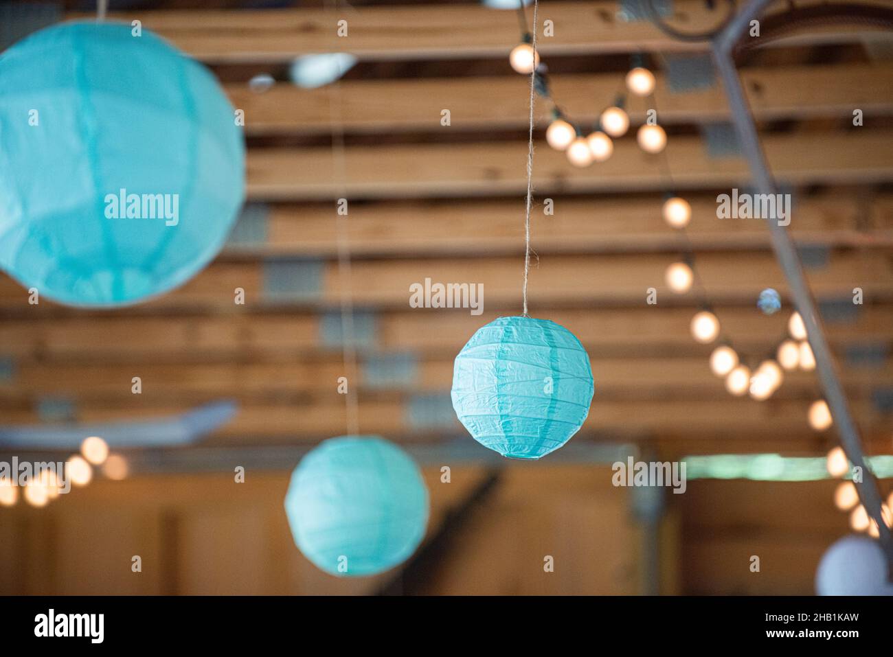 Many Blue round paper lanterns hanging from wood beam ceiling with bokeh Stock Photo