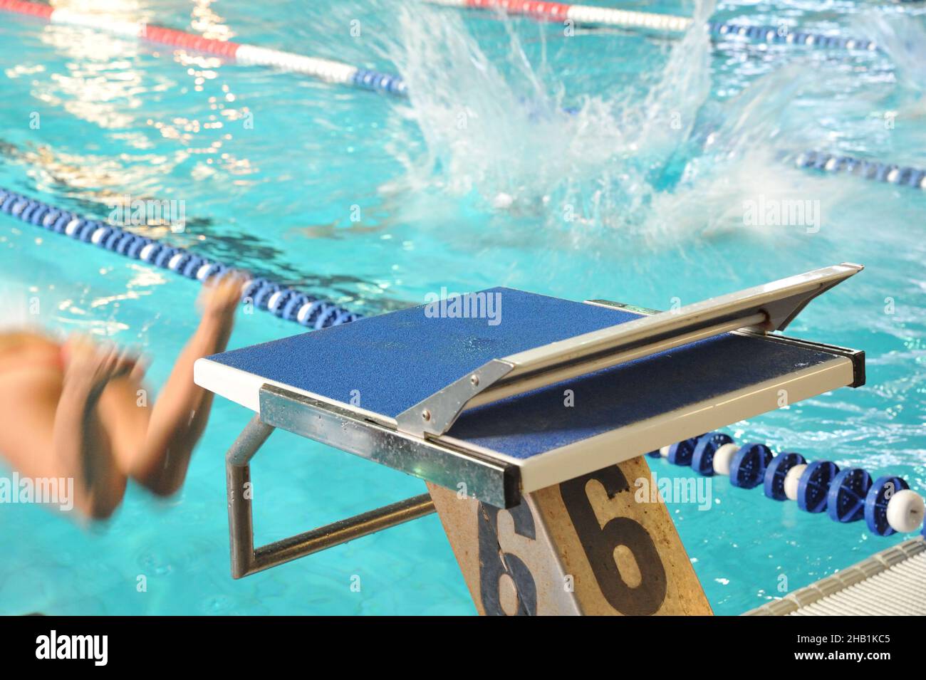 Young female jumping from a diving board into the swimming pool with a