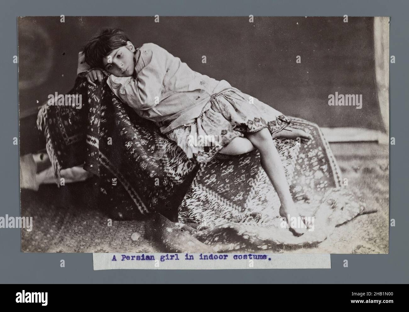 Young Girl Lying Down on Kilim, One of 274 Vintage Photographs, Albumen silver photograph, late 19th-early 20th century, Qajar, Qajar Period, 4 7/8 x 7 5/8 in., 12.4 x 19.3 cm, 19th century, black and white, carpet, child, dress, girl, historical fashion, Iran, Persian, Persian Rug, photograph, photography, rug Stock Photo