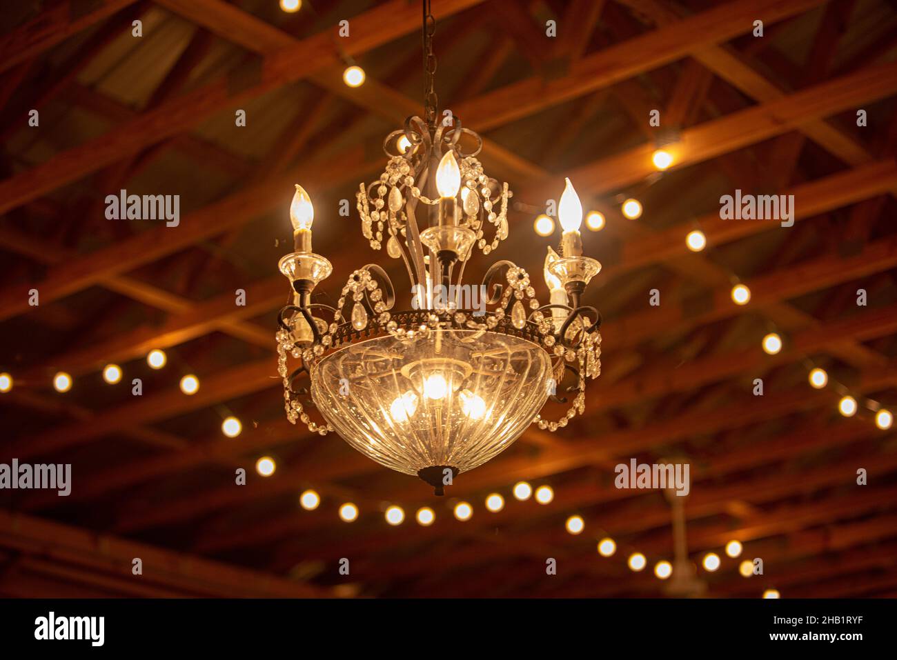Warm victorian chandeleir hanging from wood beam ceiling in a barn Stock Photo