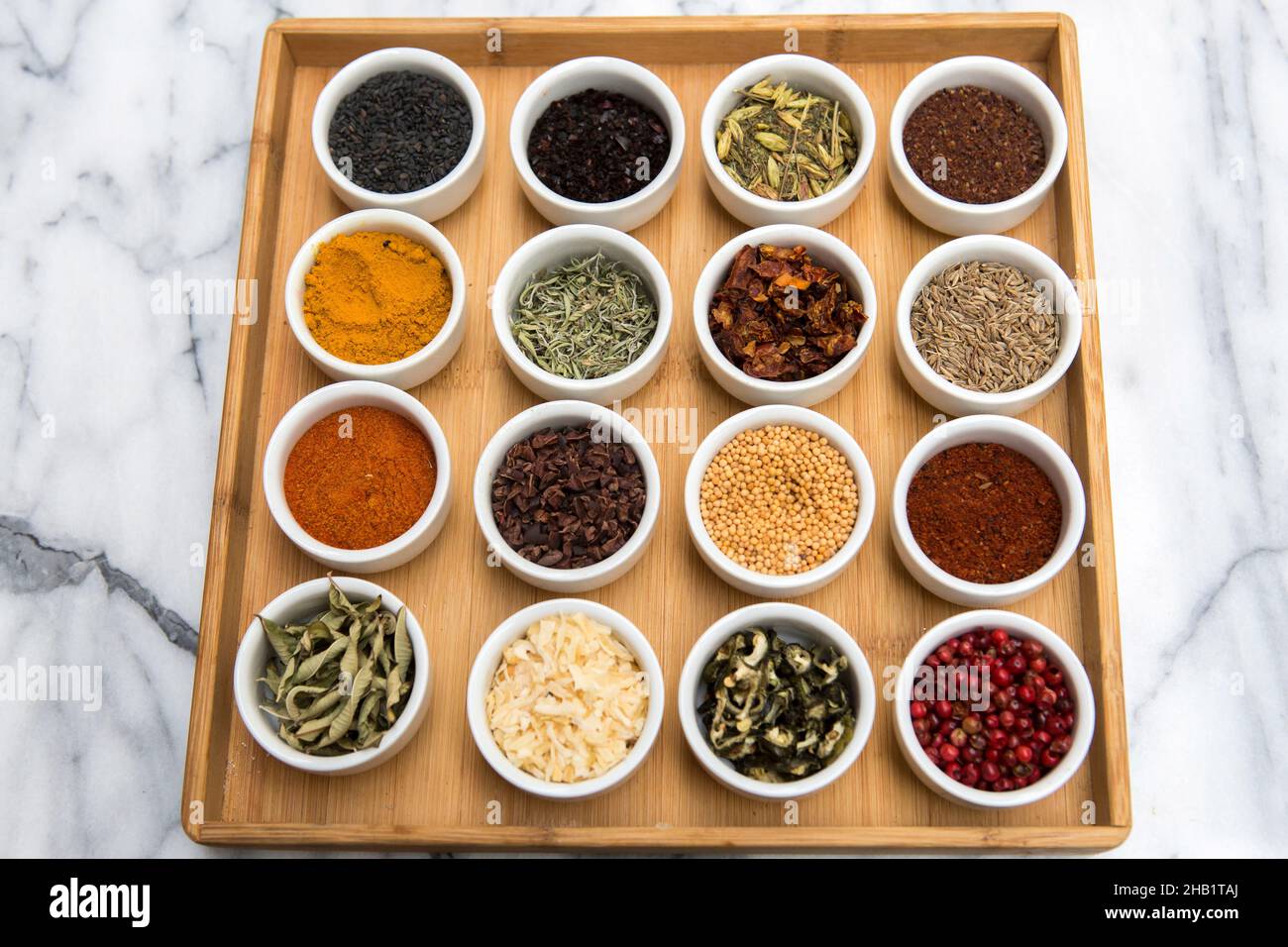 A selection of herbs and spices in small round containers displayed on a bamboo tray Stock Photo