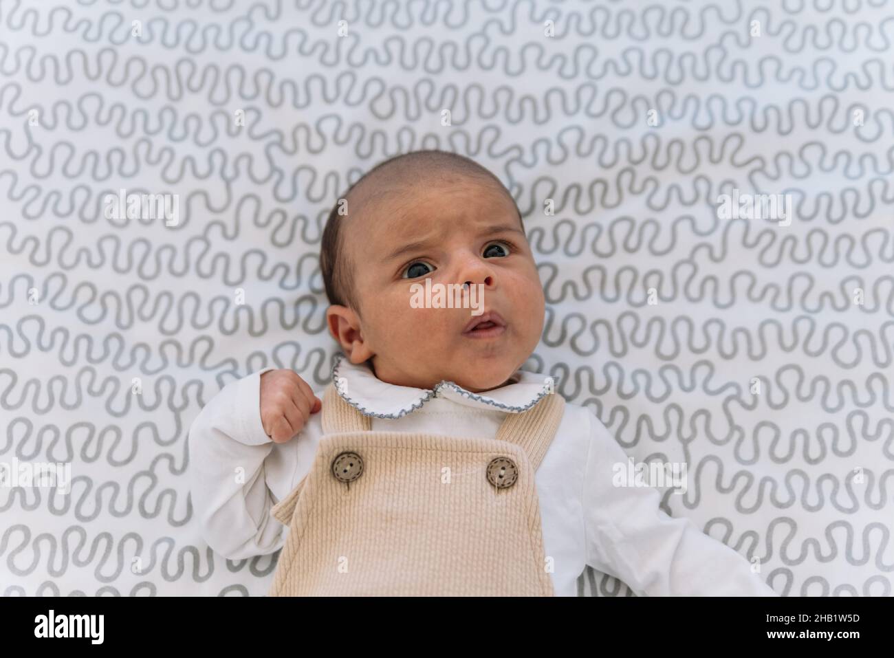 Elegant baby in suit and dungarees lying on the bed. Stock Photo