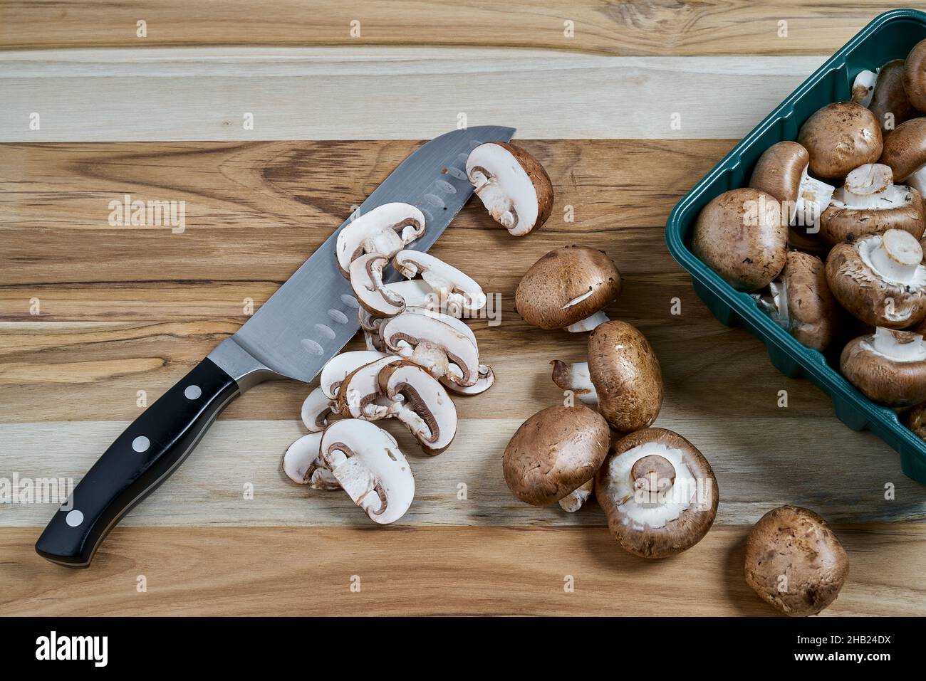 Fresh Baby Bella Mushrooms being sliced on wood kitchen countertop
