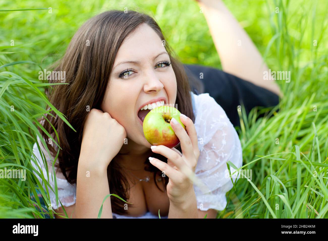 Apple, lying, woman, meadow, bite, bite, teeth, face, apple, bite, red, Styria, person, laughing, one, Austria, leisure, looking, Leibnitz, blouse, gr Stock Photo