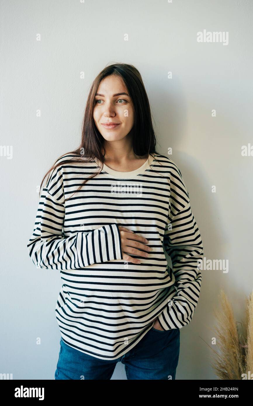 Vertical portrait of a young pregnant woman in a striped sweatshirt. Stock Photo