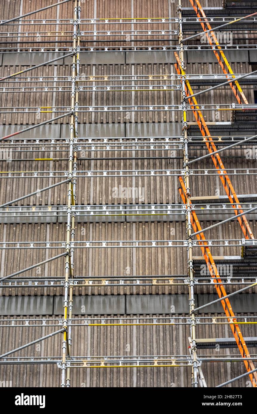 scaffolding and ladders on the side of a high rise or multi-storey block of flats or offices for essential maintenance work on the exterior cladding Stock Photo
