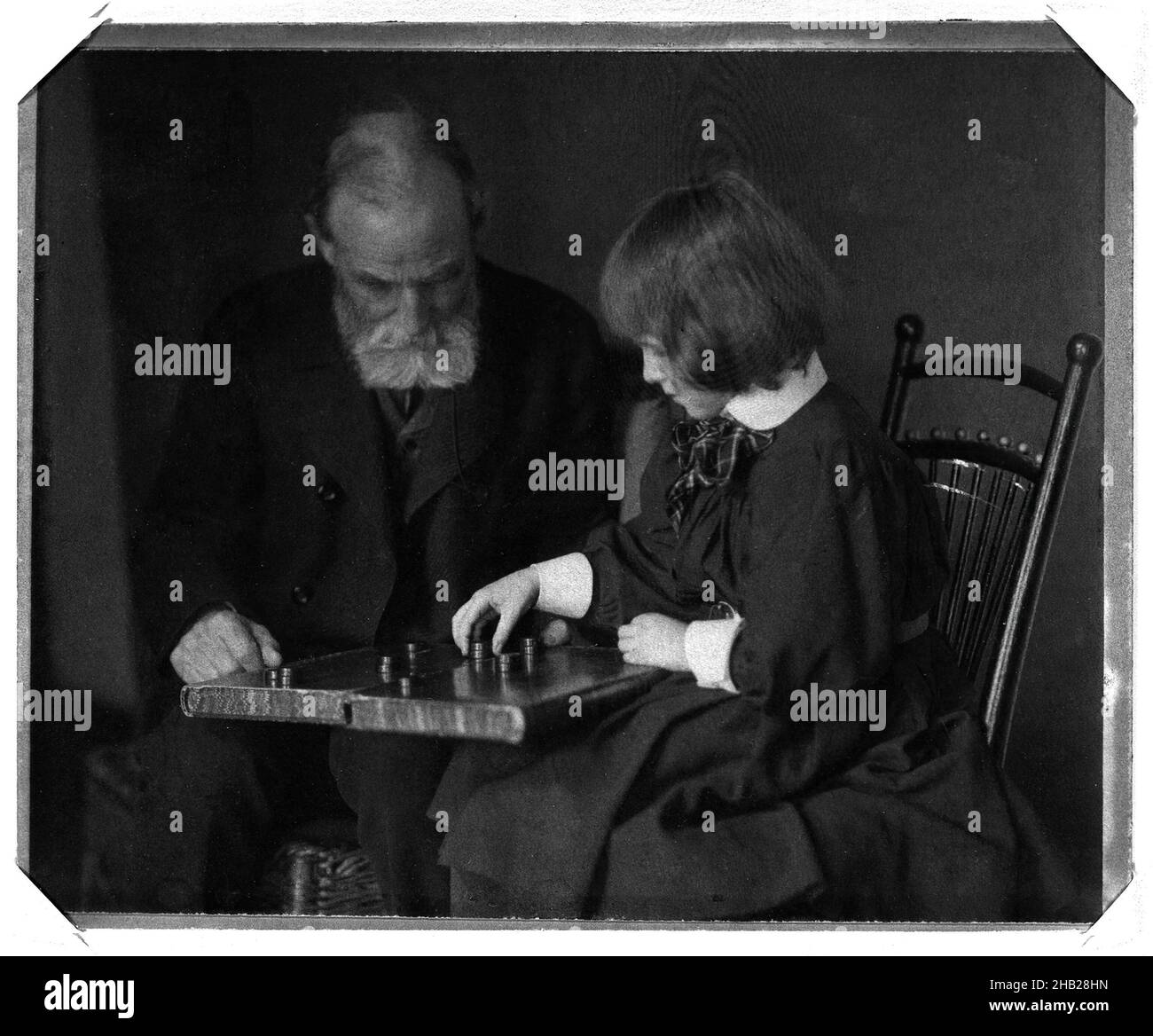 Seated Portrait of William Rand and Grandaughter Peggy Lee Playing Checkers, Gertrude Kasebier, American, 1852-1934, Platinum print, ca. 1898-1900, image: 4 15/16 x 6 1/8 in., 12.5 x 15.5 cm, beard, board game, checkers, child, early American, female photographer, games, grandchild, granddaughter, grandfather, liesure, photograph, Rand McNally, seated, woman artist Stock Photo