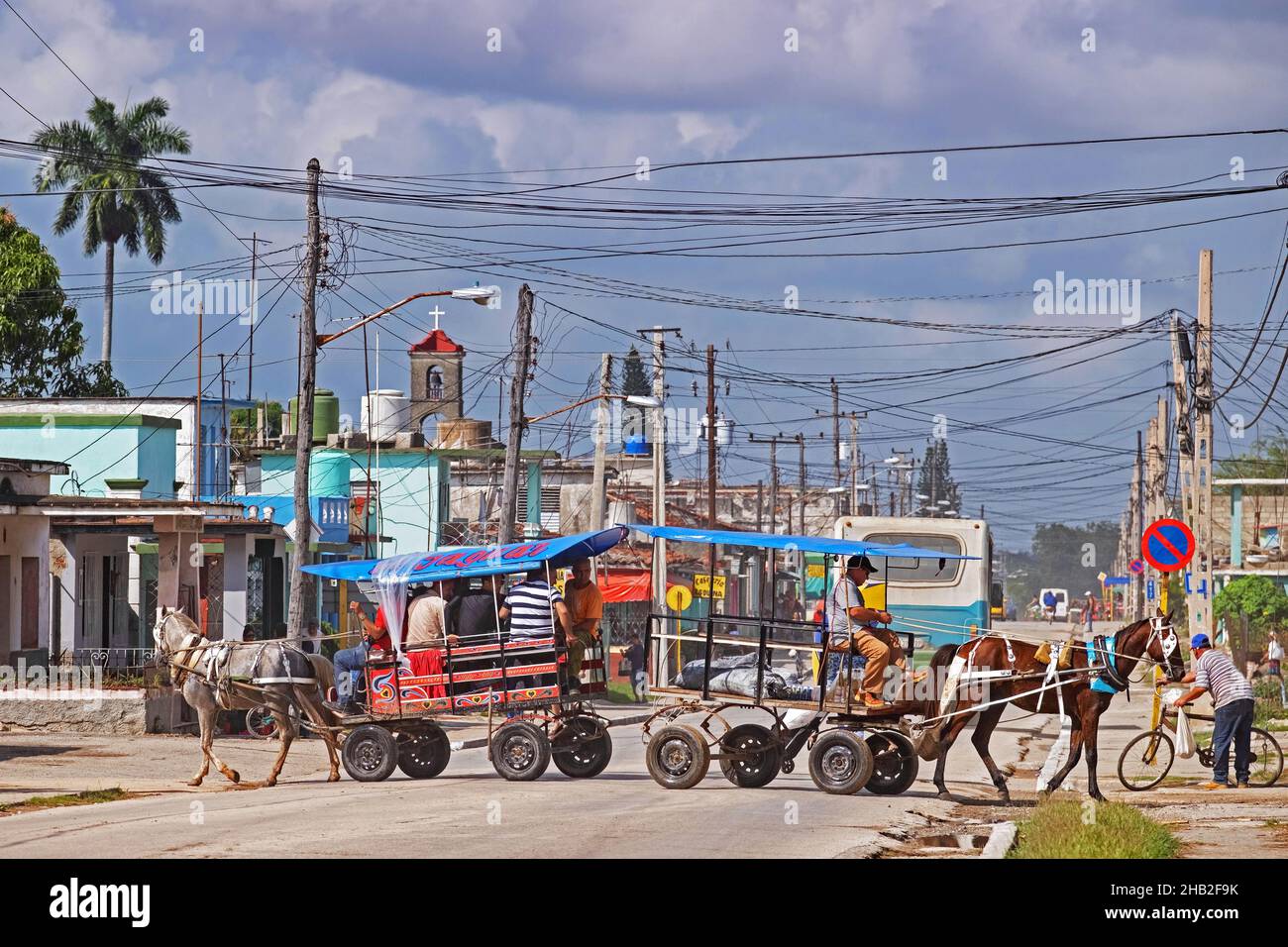 Horse-drawn carriage with passengers and horse with cart crossing road in the town Jatibonico, Sancti Spíritus Province on the island Cuba, Caribbean Stock Photo