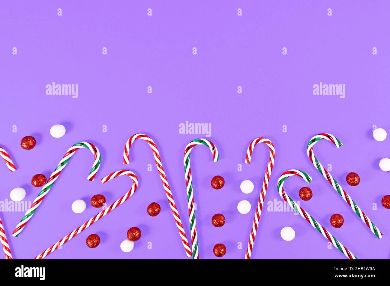 Christmas candy canes and ornament balls at bottom of purple background