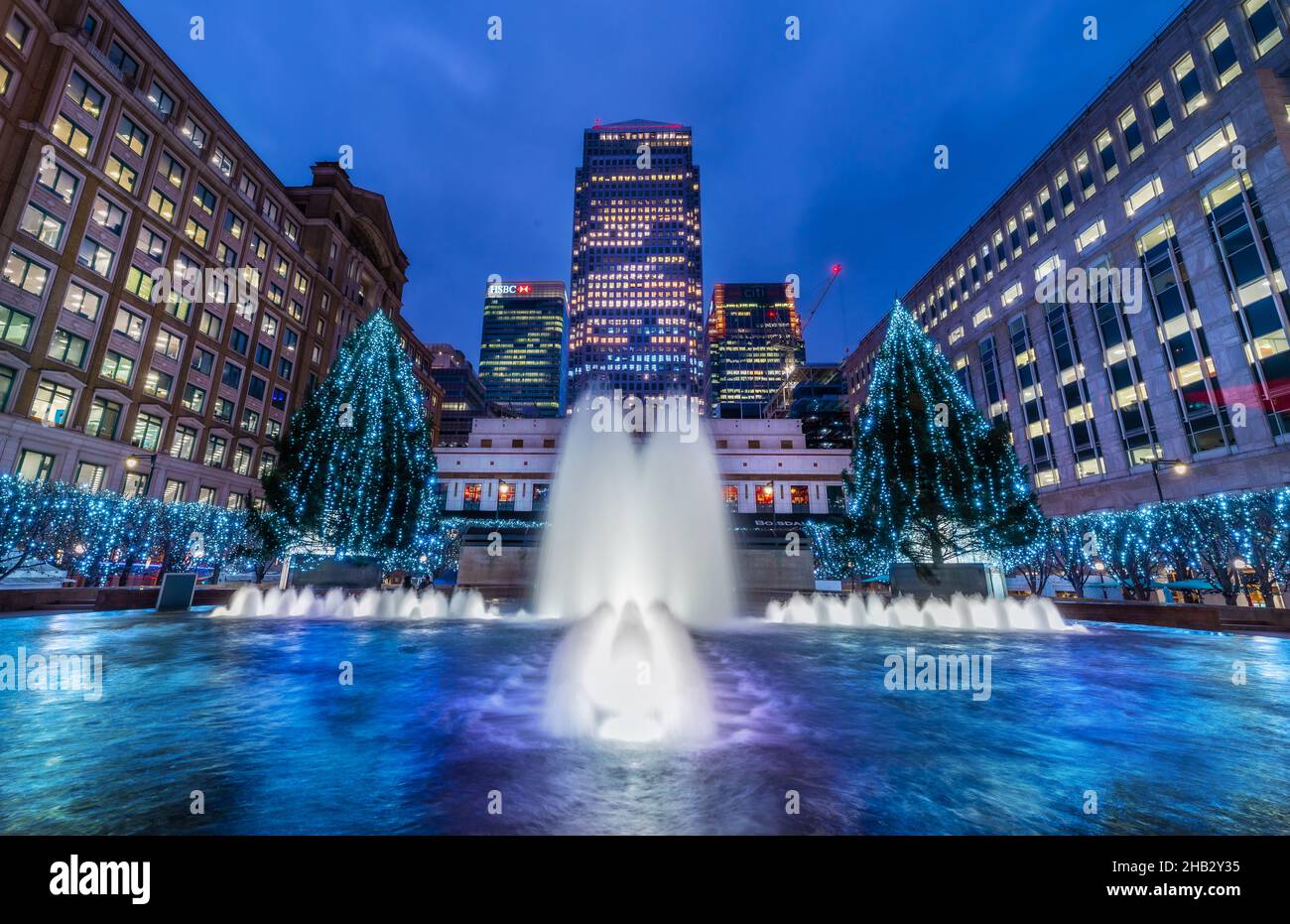 London, England, UK - December 15, 2021: Wide view of the Cabot Square and artistic fountain illuminated in evening lights, surrounded by Christmas de Stock Photo