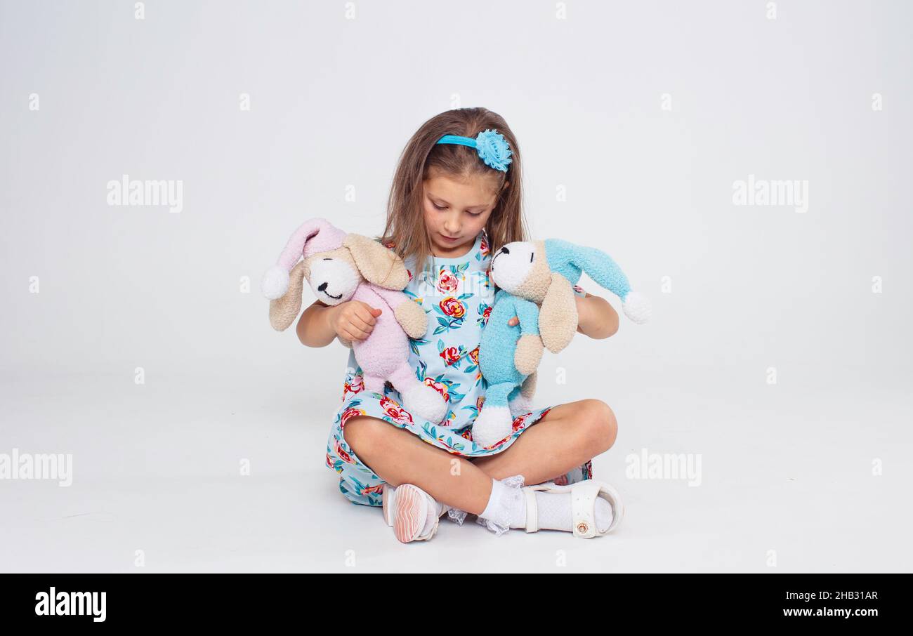 A little girl in a bright dress hugs two favorite toys on a white isolated background. Stock Photo